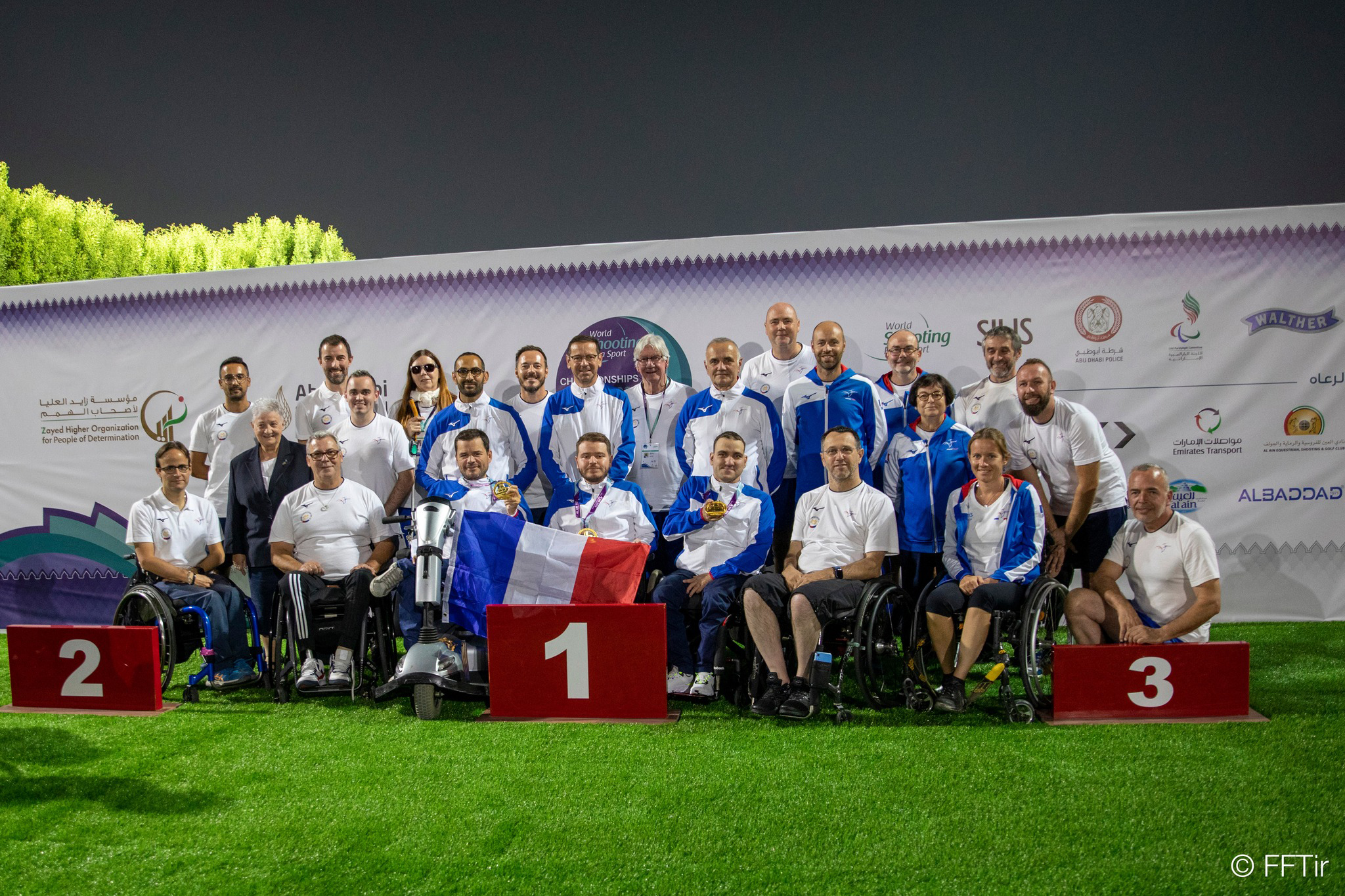 Photo: photo de l'Equipe de France aligné sur trois rang sur la pelouse du stand de tir, avec le drapeaux Français.

Photo: photo of the French team lined up in three rows on the lawn of the shooting range, with the French flag.